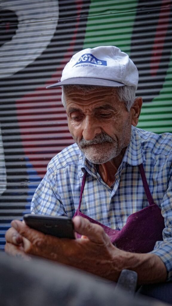 Senior man wearing cap uses smartphone against colorful shutter. Urban life captured.