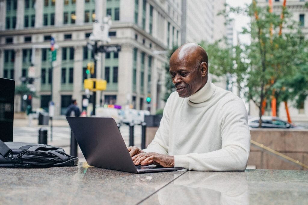 Cheerful African American male entrepreneur in casual outfit standing in downtown and working on netbook
