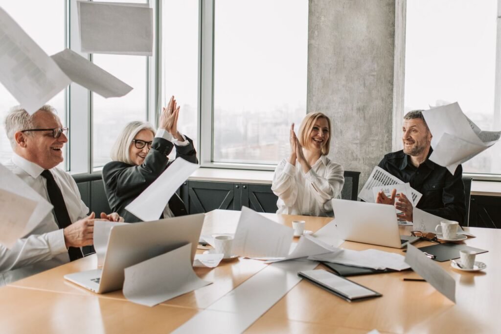 Group of happy coworkers celebrating a successful meeting, throwing papers and clapping in a modern office.